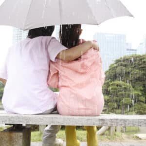 Photo of rear view of couple you are an umbrella sit on the bench in the rain for Harm Reduction workshop